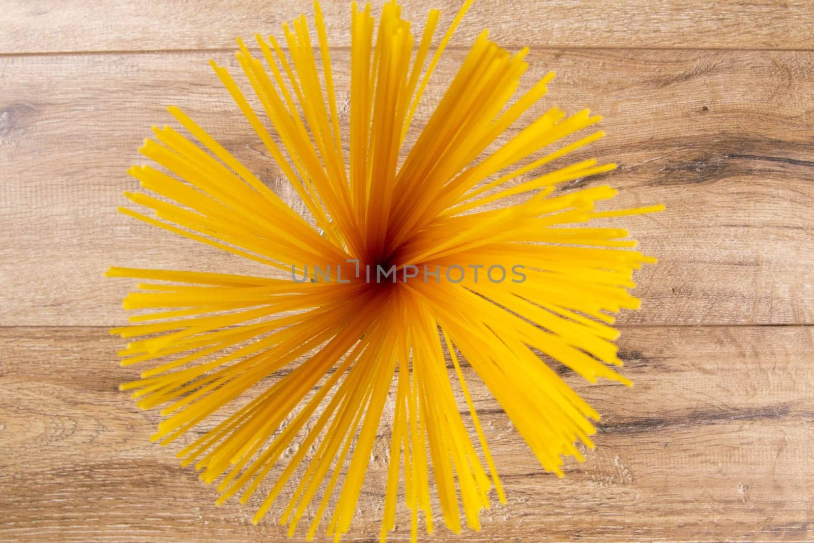 Raw spaghetti pasta inside a bowl on top of a wooden table and background with wooden cabinet.
