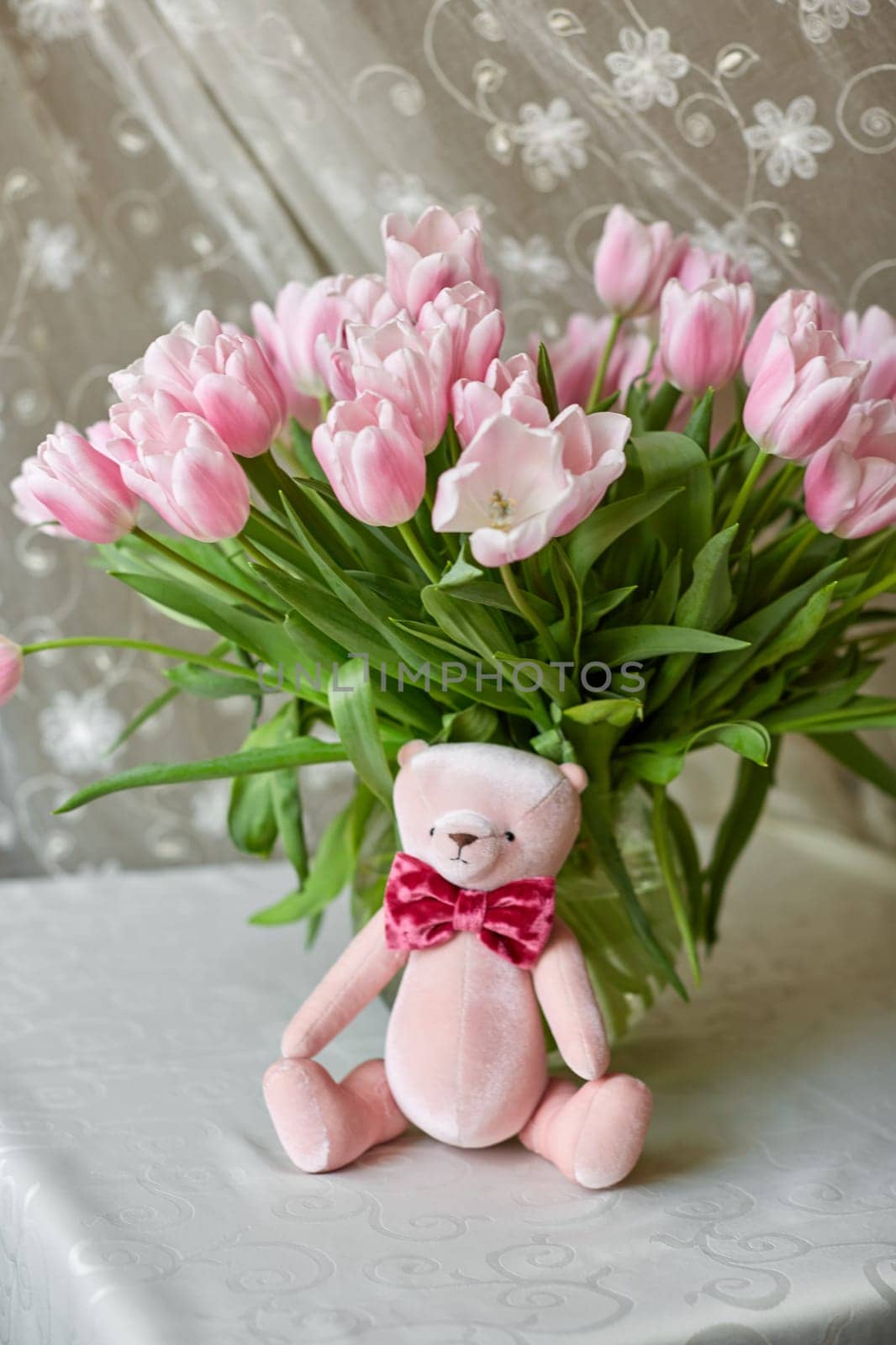 Pink bear toy and a vase with pink tulips on a table. Decor. Selective focus.