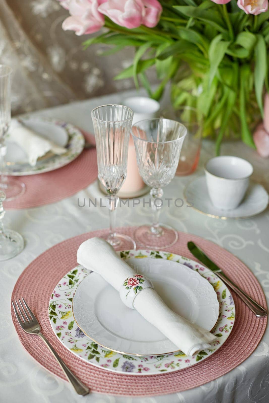 Decor and spring table setting is a vase with pink tulips and dishes of white color. Selective focus.