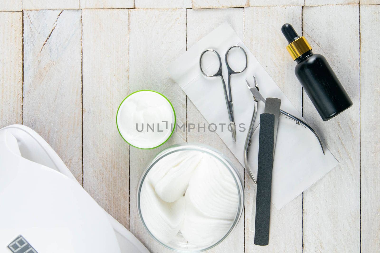 A set of cosmetic tools for manicure and pedicure on a blue background. Cuticle cutters, manicure scissors and hand oil stand on a white towel that stands on a white wooden table top view with clear space.