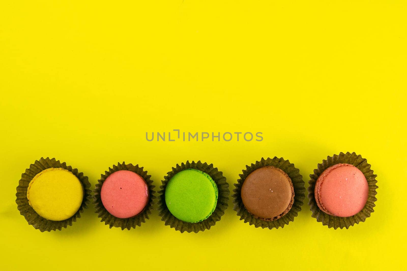 Colorful macaroons in a beautiful brown wrapper stand on a yellow background. Top views with clear space