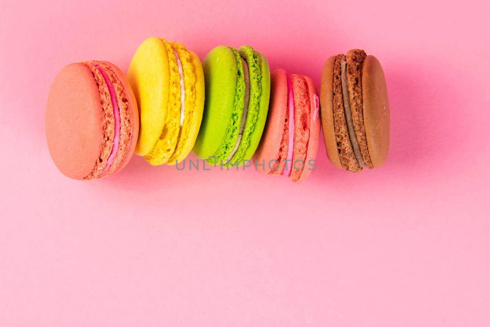 Colorful macaroons stand on a pink background. Top views with clear space