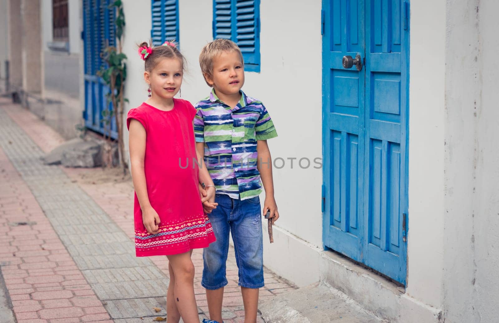 Kids walking by the street next to shutter blue window
