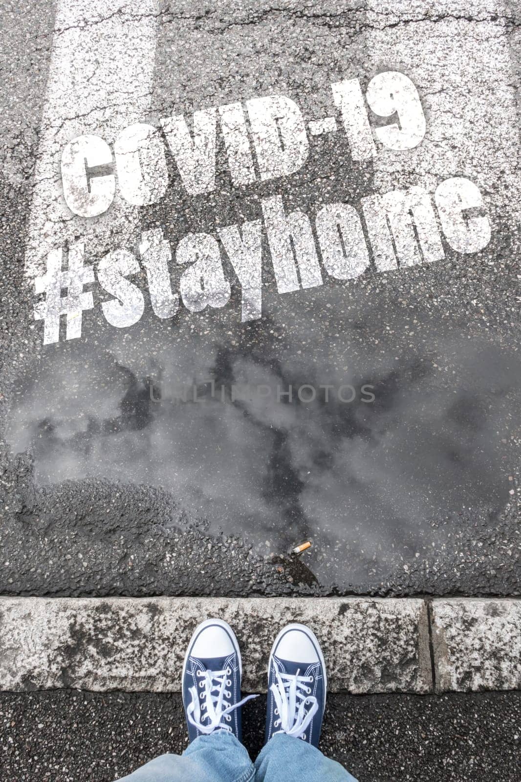 Feet of a man in sneakers shoes standing on gray sidewalk with hashtag #stayhome (COVID-19). Coronavirus in the world. COVID-19 alert banner. 2019 Coronavirus concept, for an outbreak occurs in Wuhan - China.