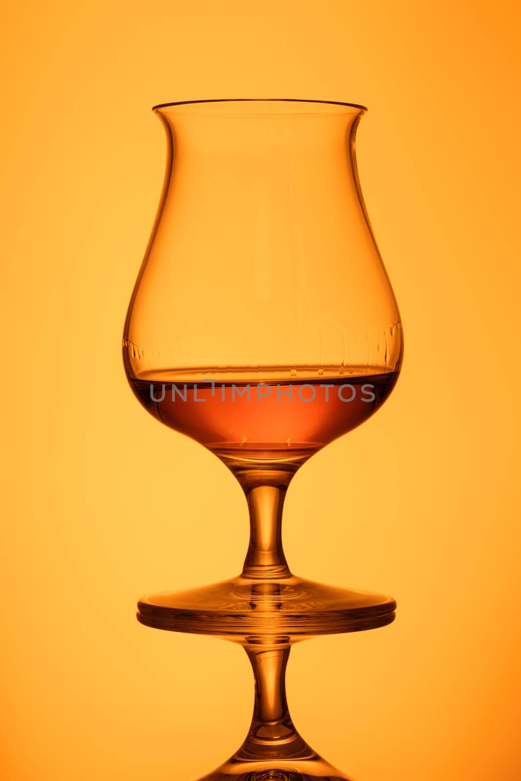 Glass with orange whisky in back lit with reflection