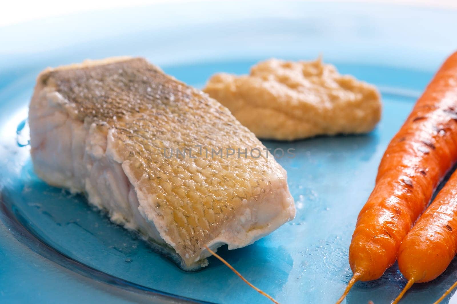 Pike perch with skin and carrots and hummus on a glass plate