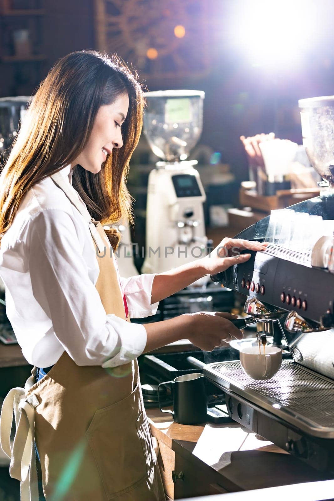 Side view shot of a barista brewing coffee by modern coffeemaker machine to making a cup of coffee with other barista working in background. Using for small business entrepreneur owner concept.