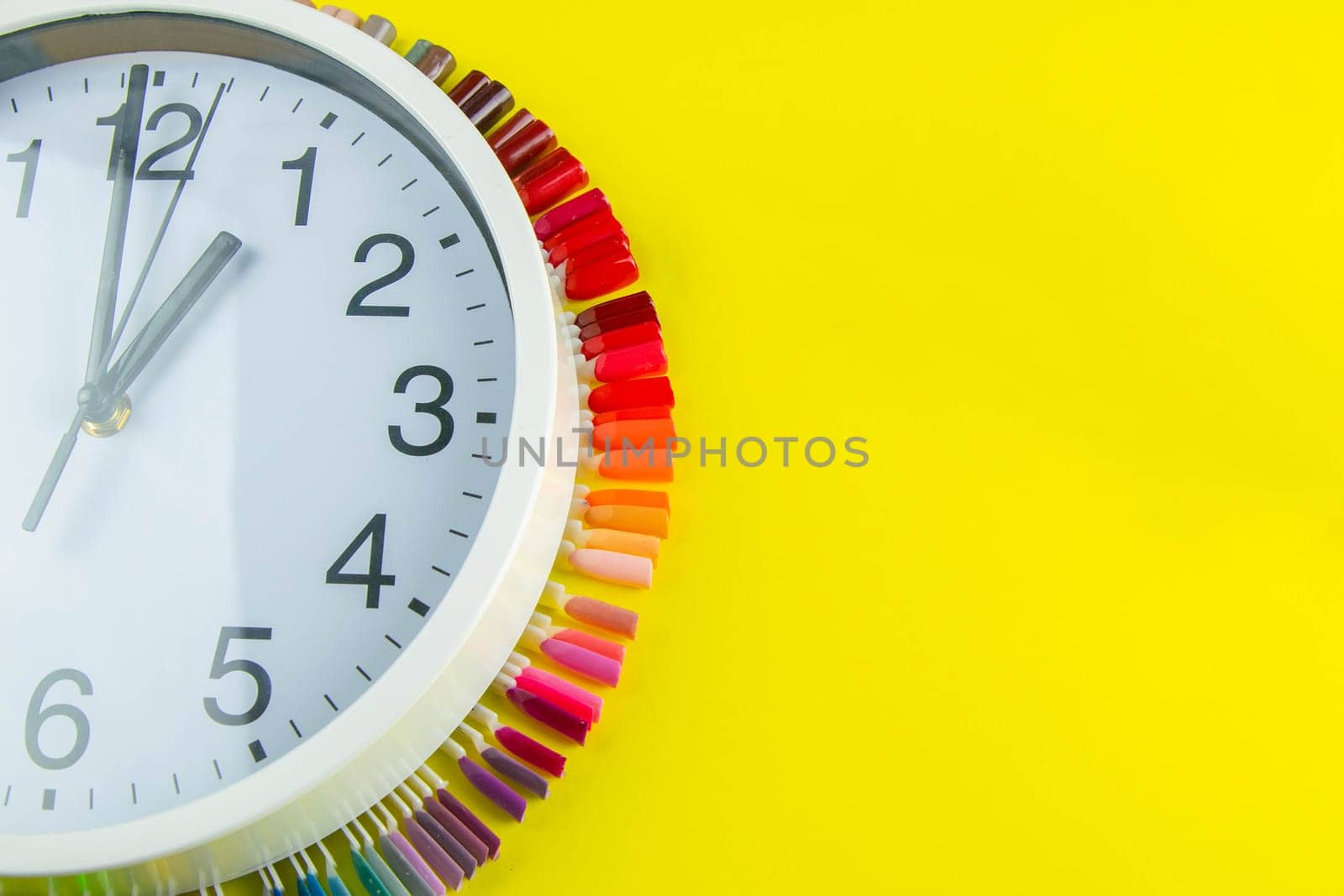 A set of cosmetic tools for manicure and pedicure on a blue background. The watch and palette of colors for manicureons on tips stands under the clock all standing on a yellow background.