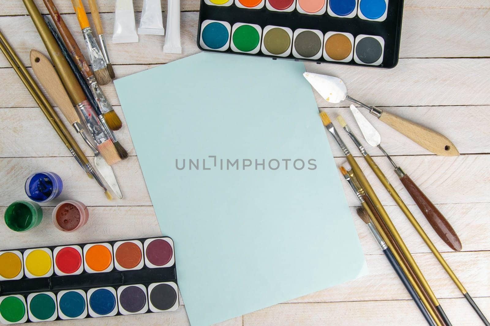Set of artist accessories collection. Canvas, tube of oil paint, art brushes, palette knife and blue paper lying on the wood table. Artist workshop background.