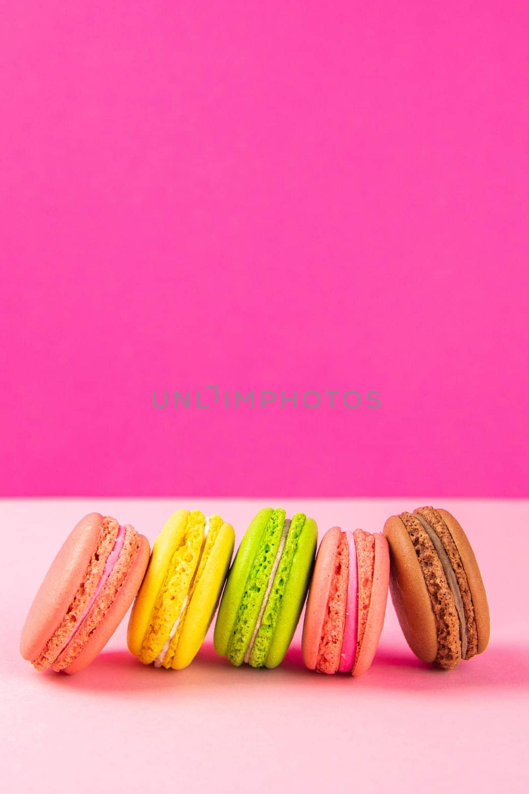 Colorful macaroons stand in a row against a pink background. Close-up with clear space