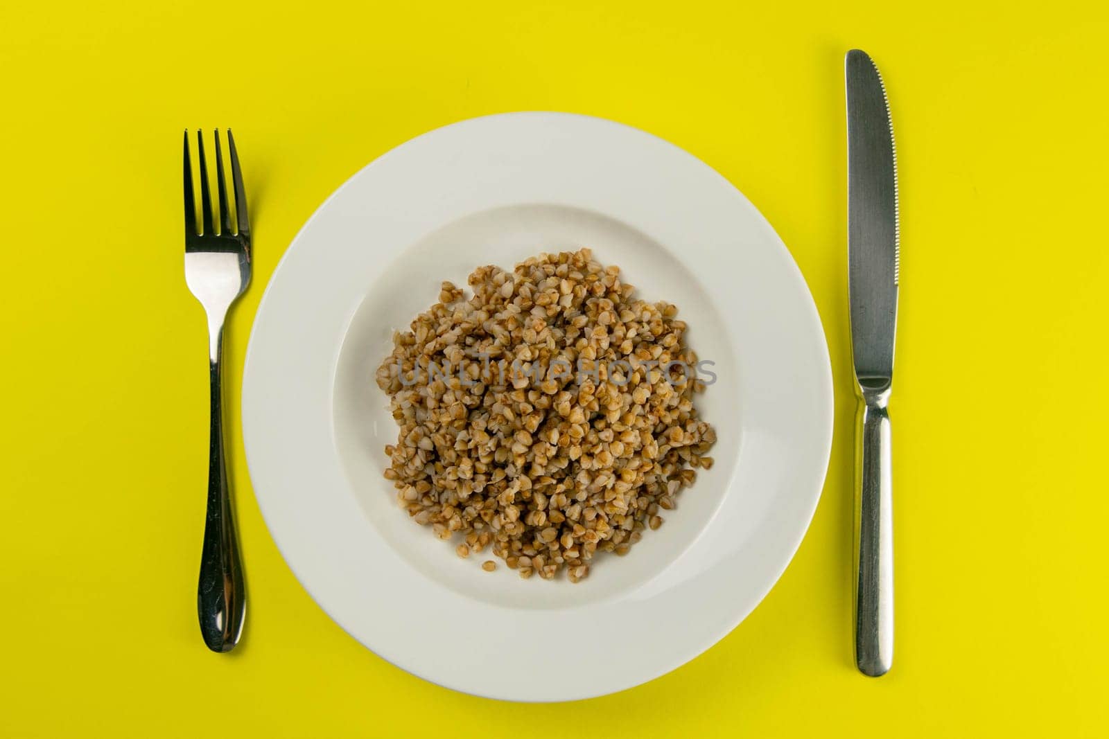 Buckwheat groats on a white plate isolated on yelllow background. Top views
