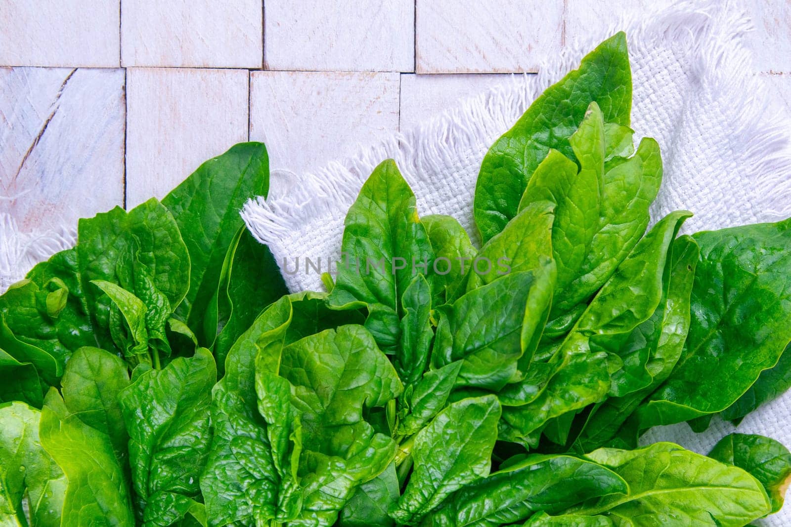 Freshly harvested spinach on a white towel, stand on white wooden table. Top views.