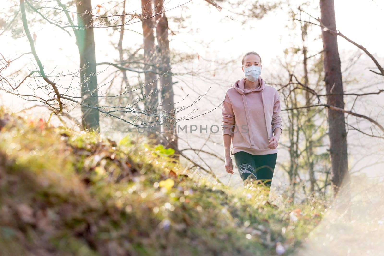 Portrait of caucasian sporty woman wearing a medical protection face mask while walking in the forest. Corona virus, or Covid-19, is spreading all over the world.