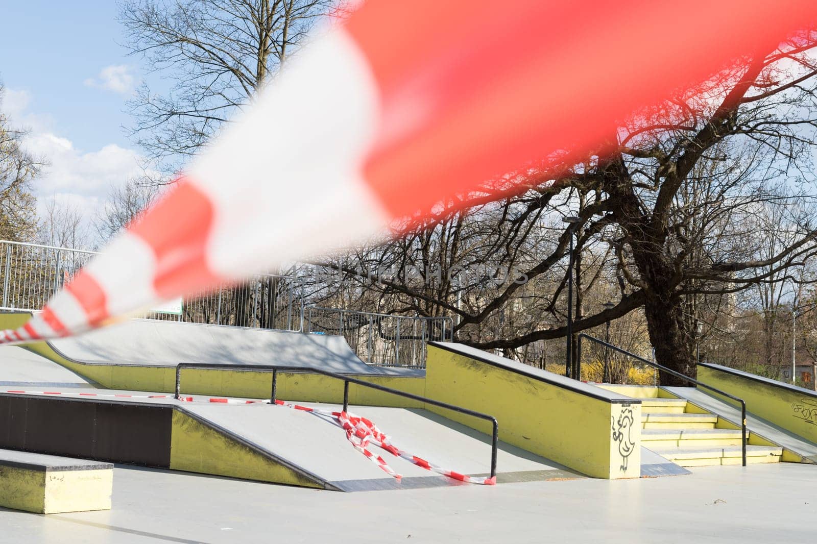 Corona virus COVID-19 restriction. No people due to quarantine. Closed urban skate park. Empty park and playground. Stay at home compaign. Red warning tape on ramps and slides. Social distancing.