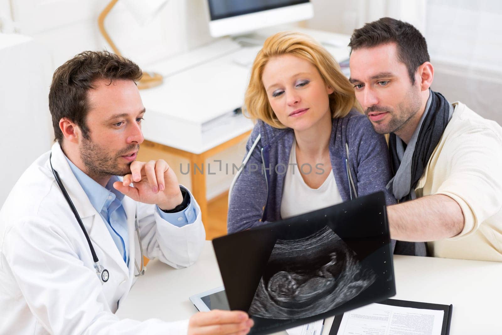 View of a Doctor shows an ultrasound to a young happy couple