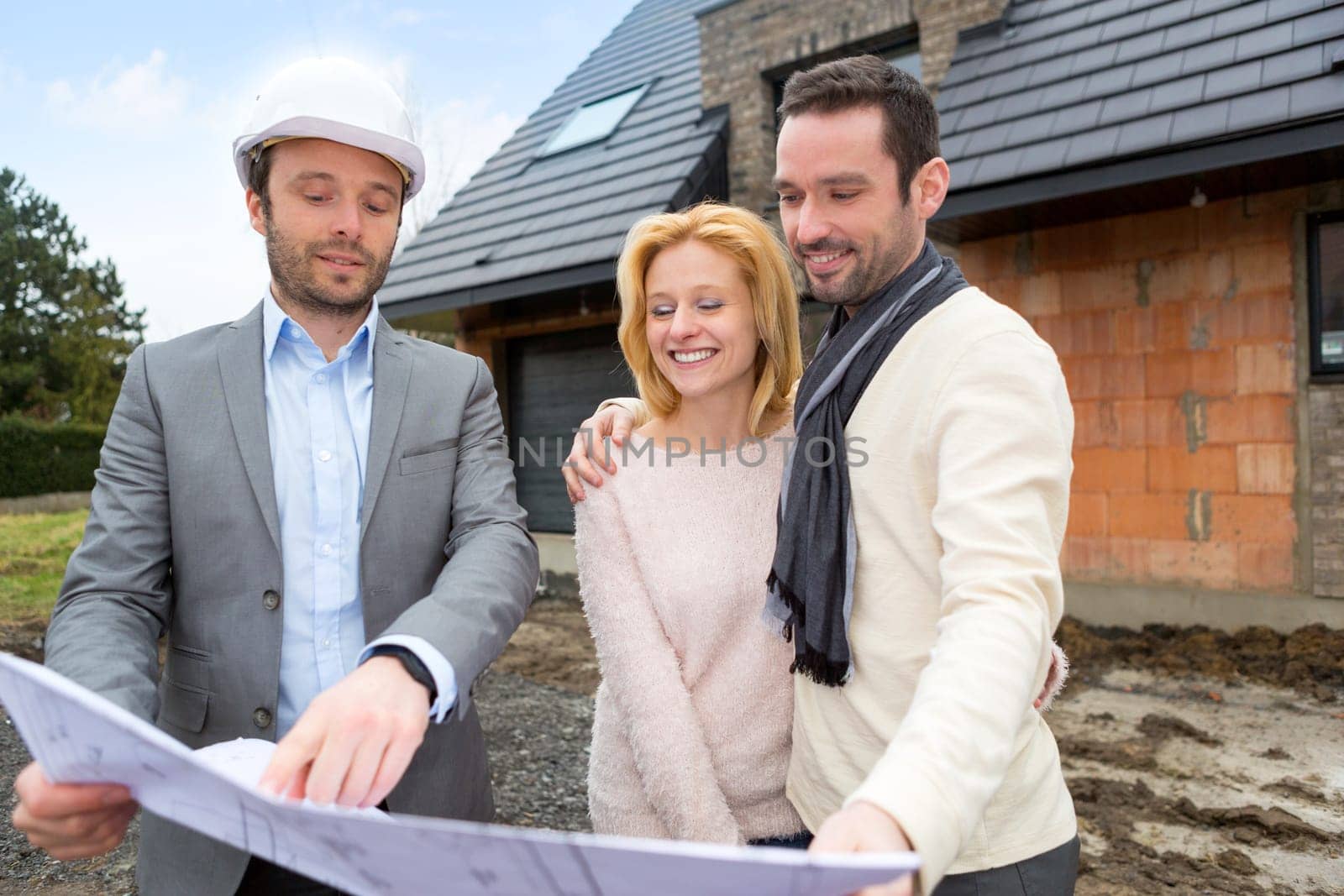 View of a Real estate agent and a young couple in front of future home