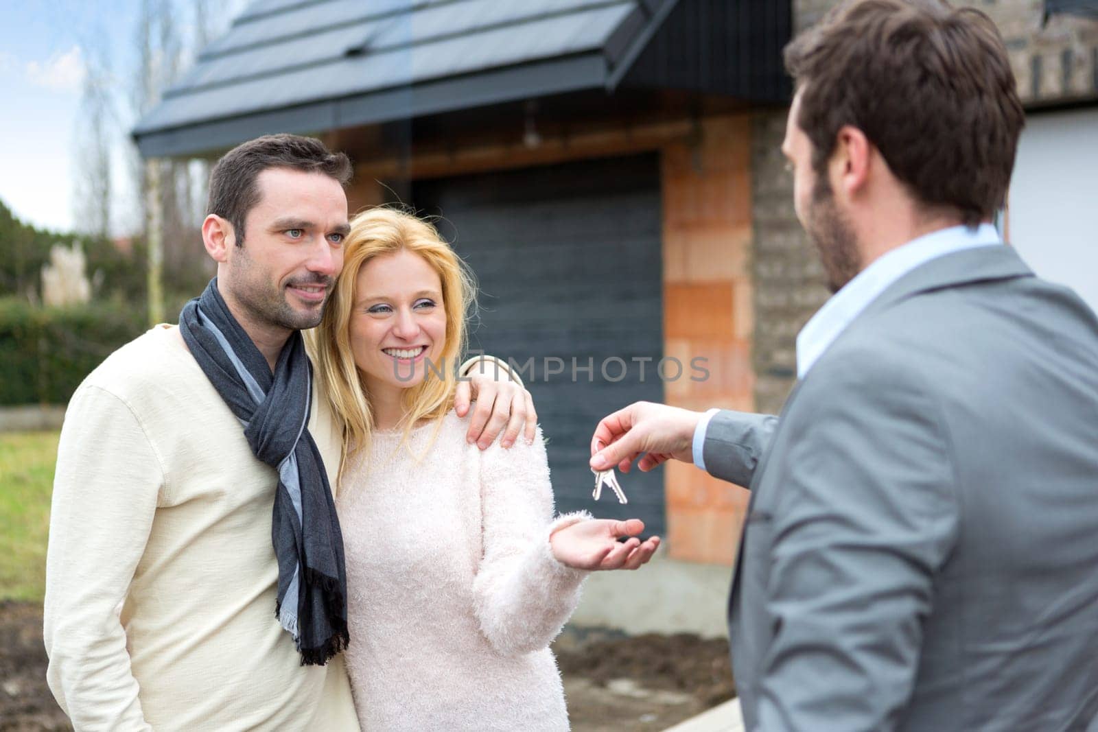 View of a Real estate agent delivers keys to young atractive couple