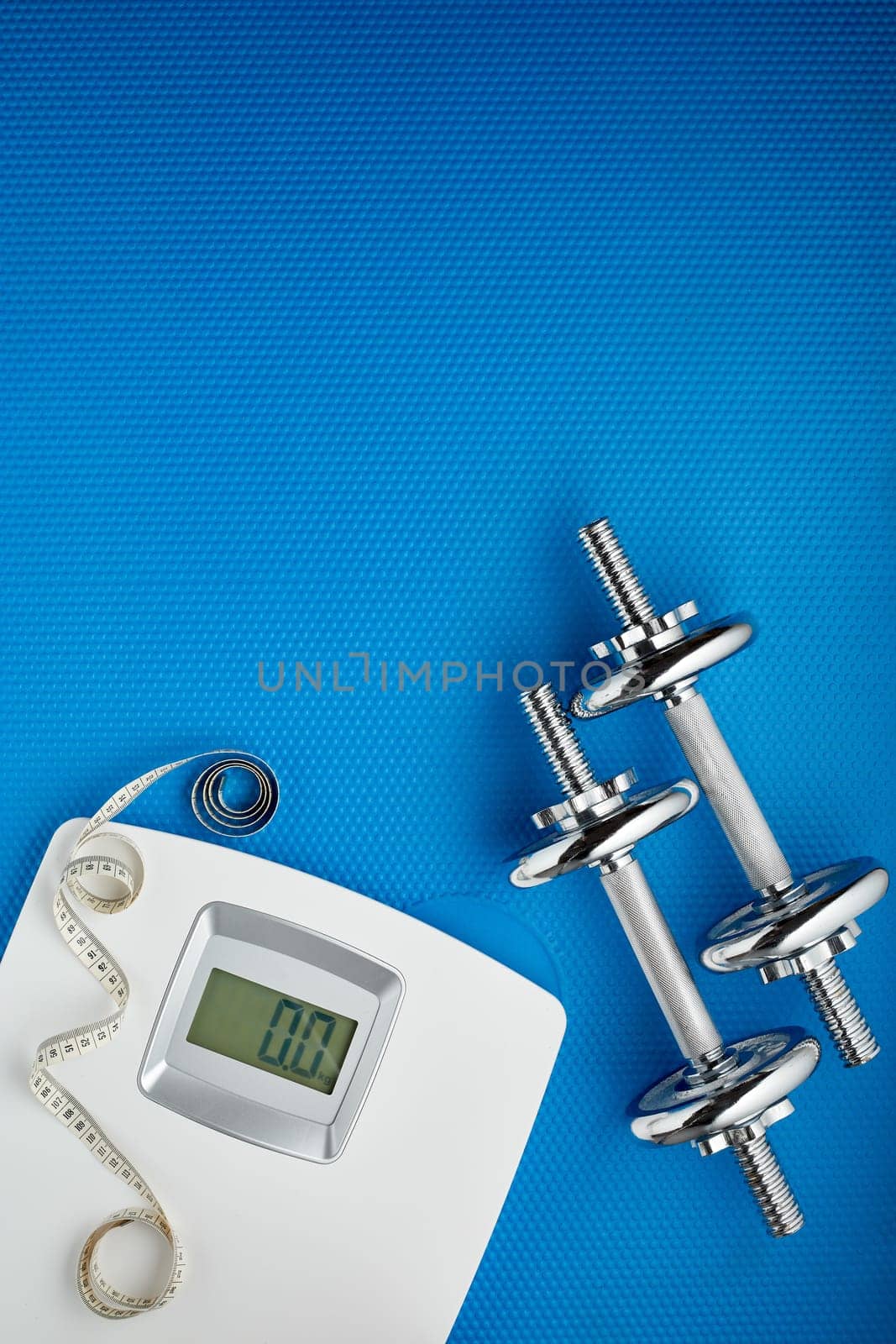 Dumbbells and scales on blue background. Planning of diet and trainings. Top view with copy space. Slimming. Sports bodybuilding equipment. Fitness, sport or healthy lifestyle concept.