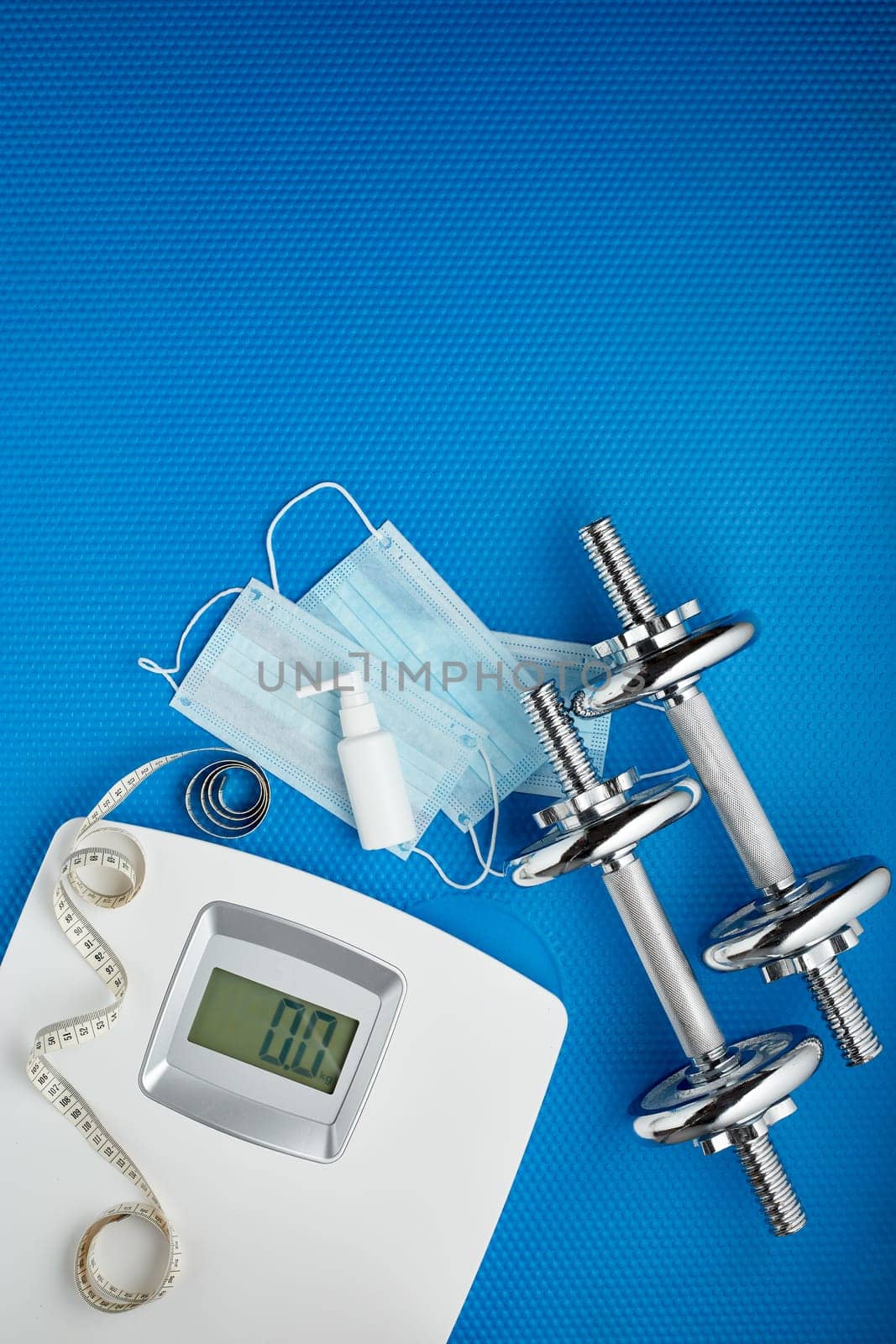 Sport equipment, scales, medical masks and sanitizer on blue background. Top view, copy space. Fitness.  Isplation period. Weight and health control during quarantine. Concept of covid or coronavirus