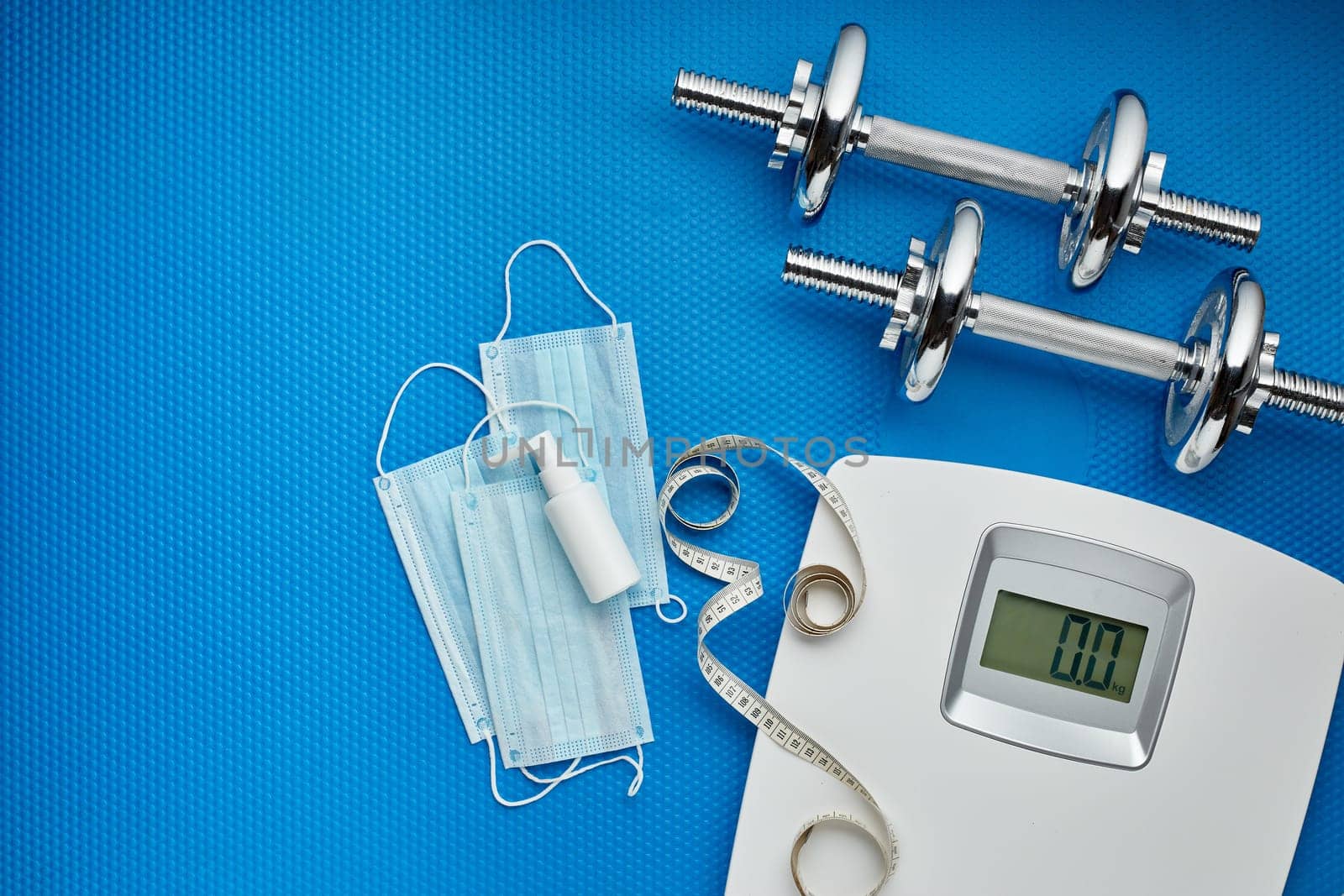 Sport equipment, scales, medical masks and sanitizer on blue background. Top view, copy space. Fitness.  Isplation period. Weight and health control during quarantine. Concept of covid or coronavirus