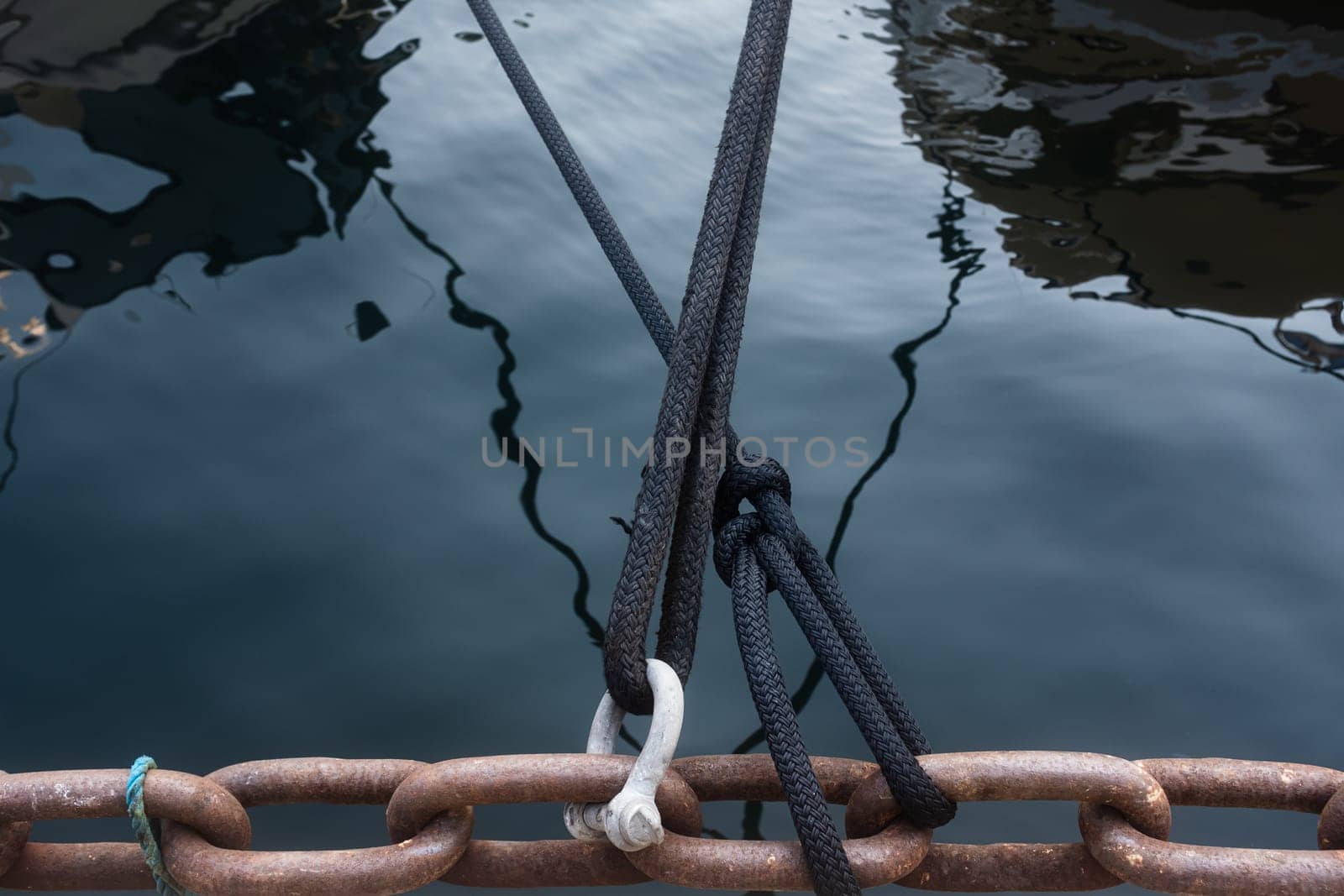 Detail of two mooring ropes crossing before tightening to a large chain in the pier and reflections of luxury yachts in the water.
