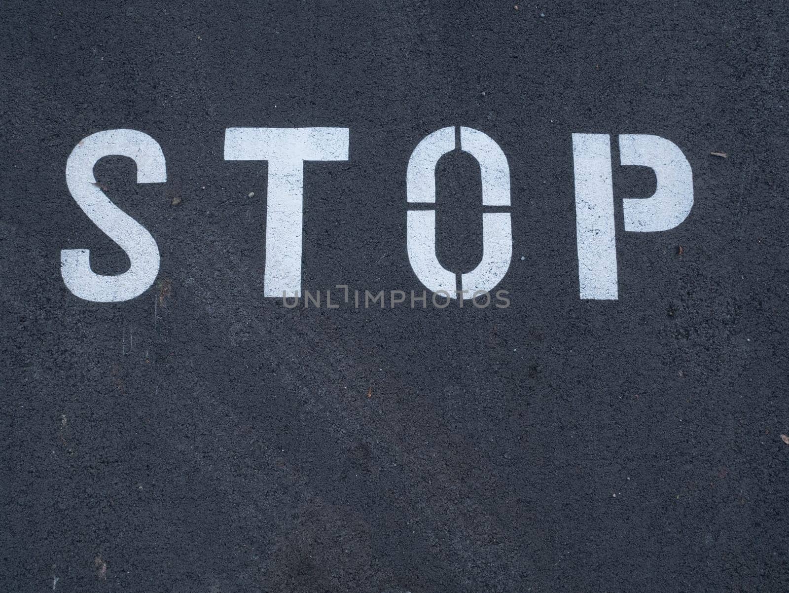 White stop sign painted on dark asphalt. You can see tire tracks over it. Indicates a mandatory stop.