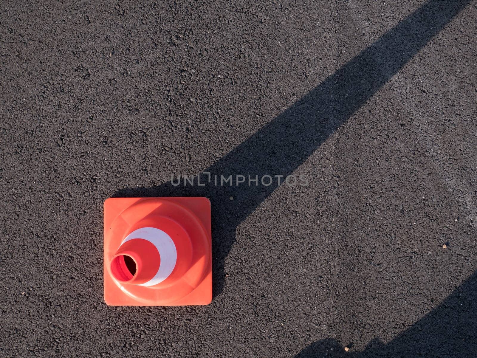 Traffic cone with shadow on asphalt. Traffic cone, with white and orange stripes on gray asphalt, copy space.