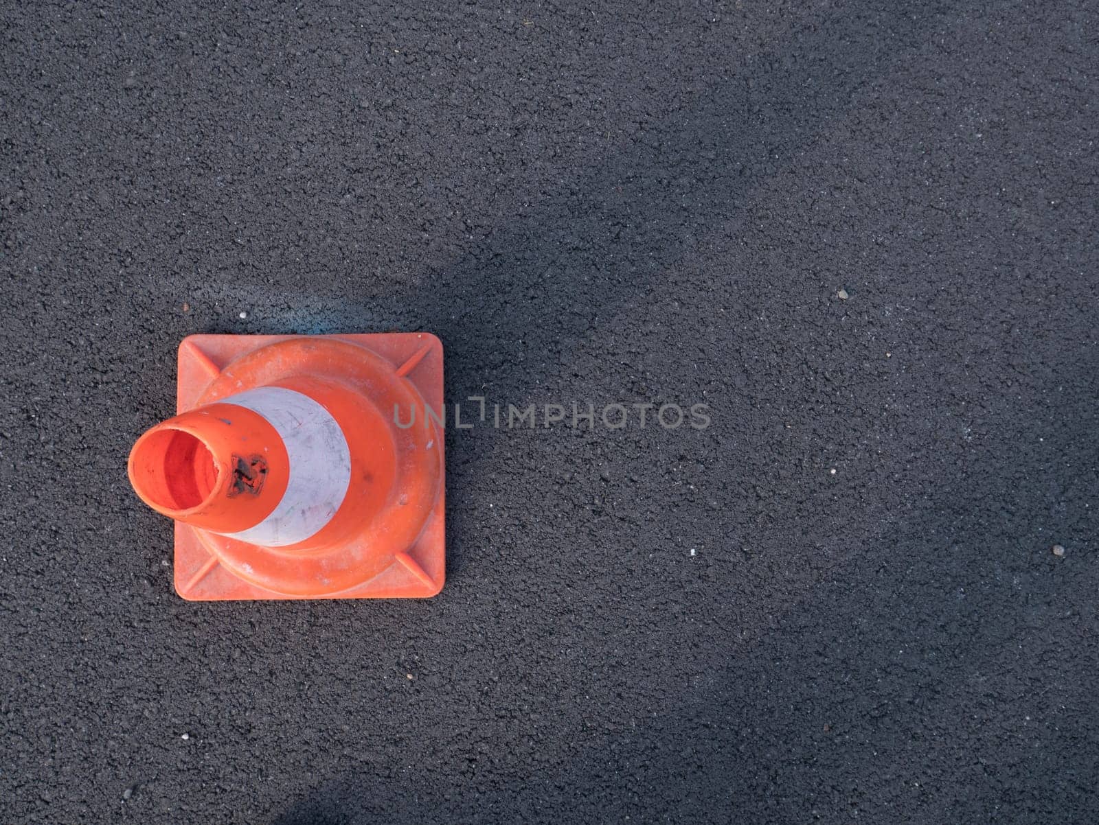 Traffic cone with shadow on asphalt. Traffic cone, with white and orange stripes on gray asphalt, copy space.