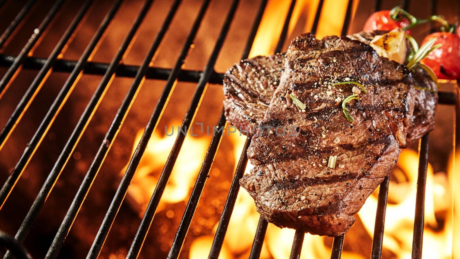 Two portions of thick tender seasoned grilled beef steak on a BBQ grill keeping warm over the hot coals in a panorama banner with copy space