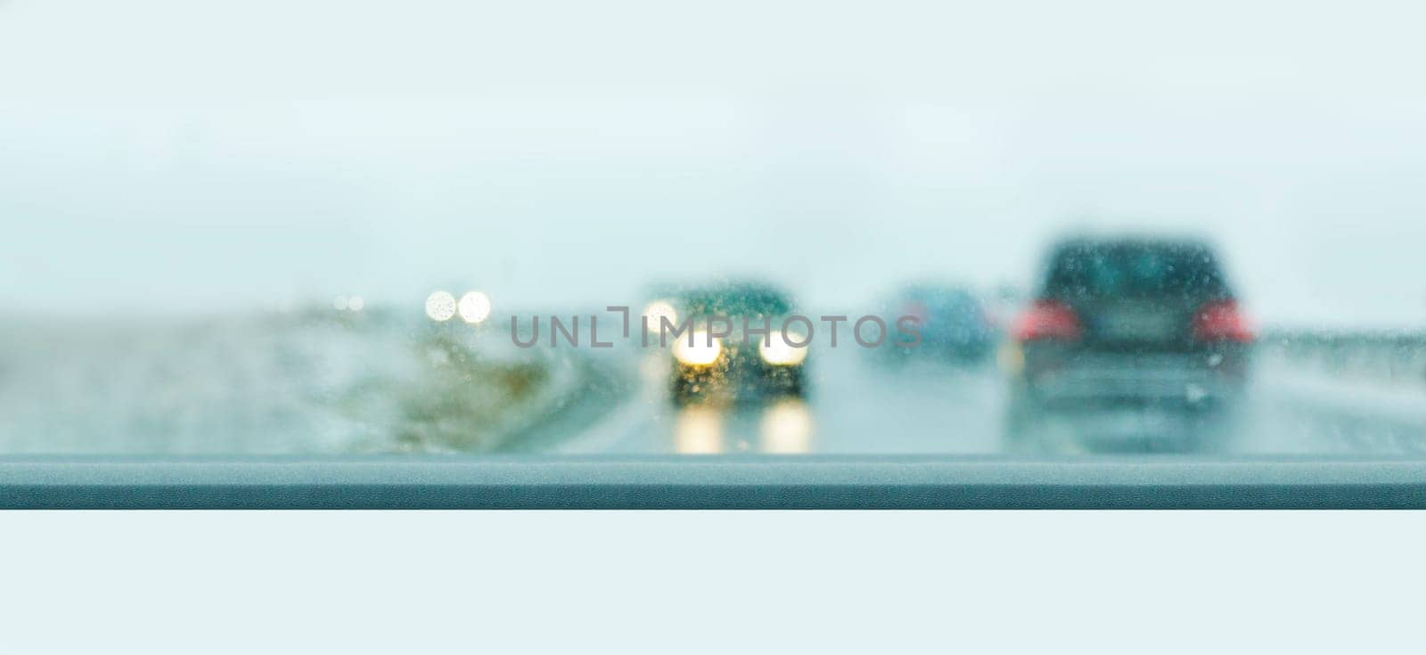 Car traffic on a rainy day seen through a wet windshield.