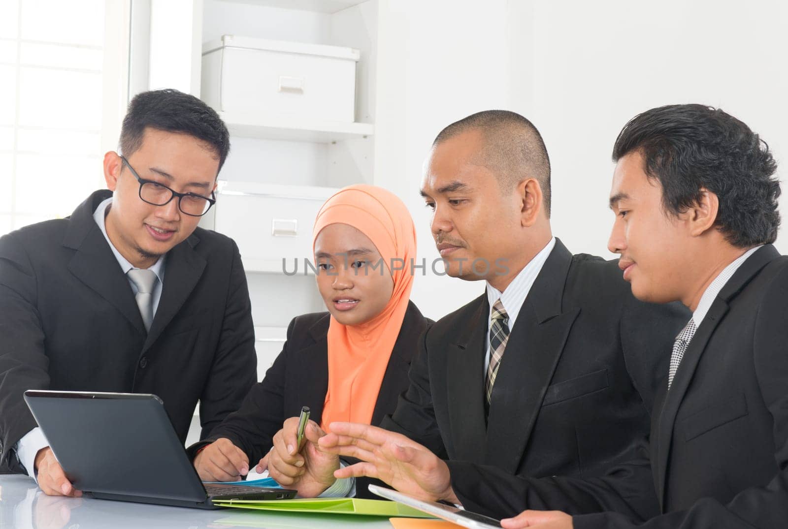 Group of Malaysian businesspeople meeting or having discussion on desk inside office room.