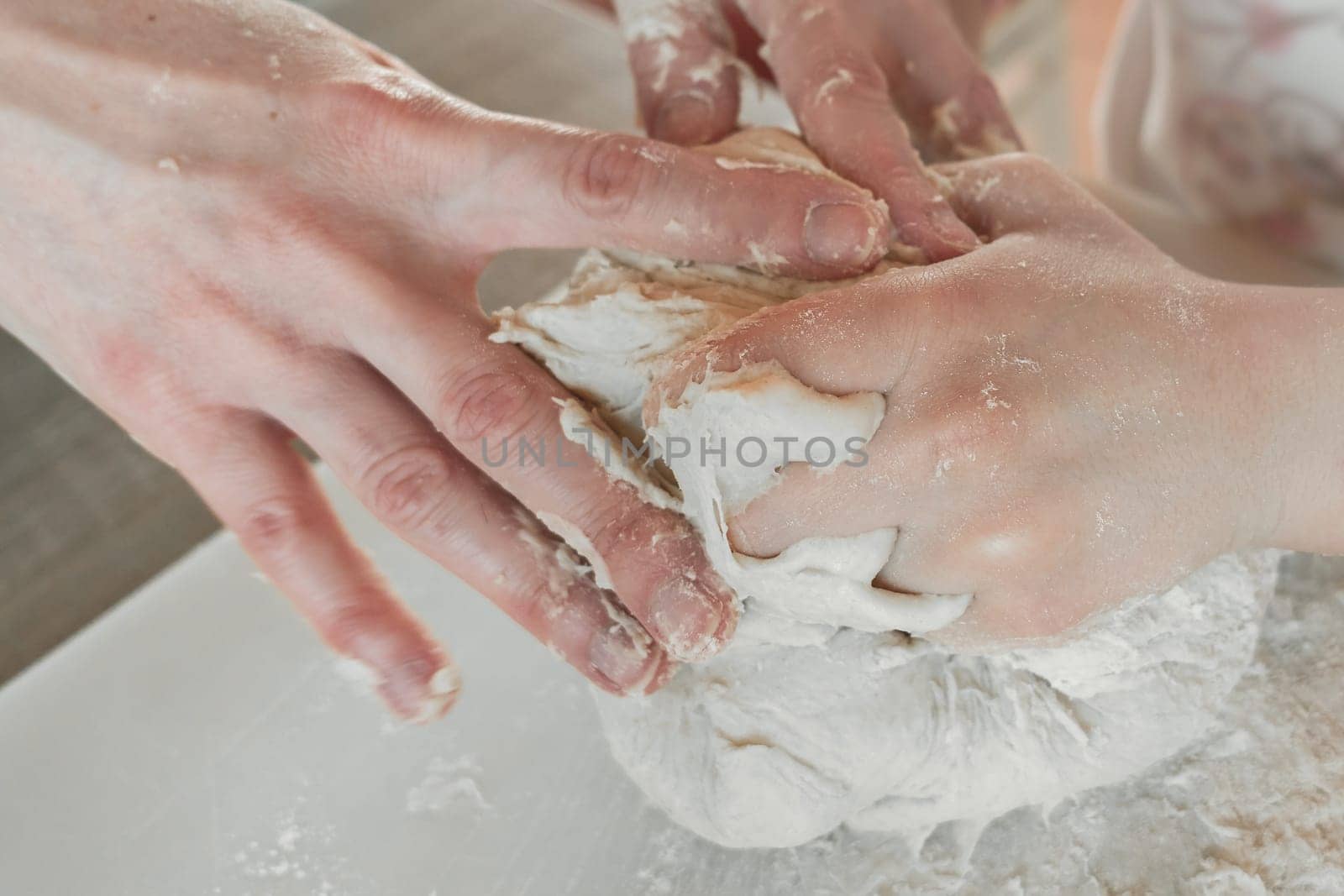 Hands of mother and daughter knead dough for pizza and bread. Having fun together in kitchen. Close-up.