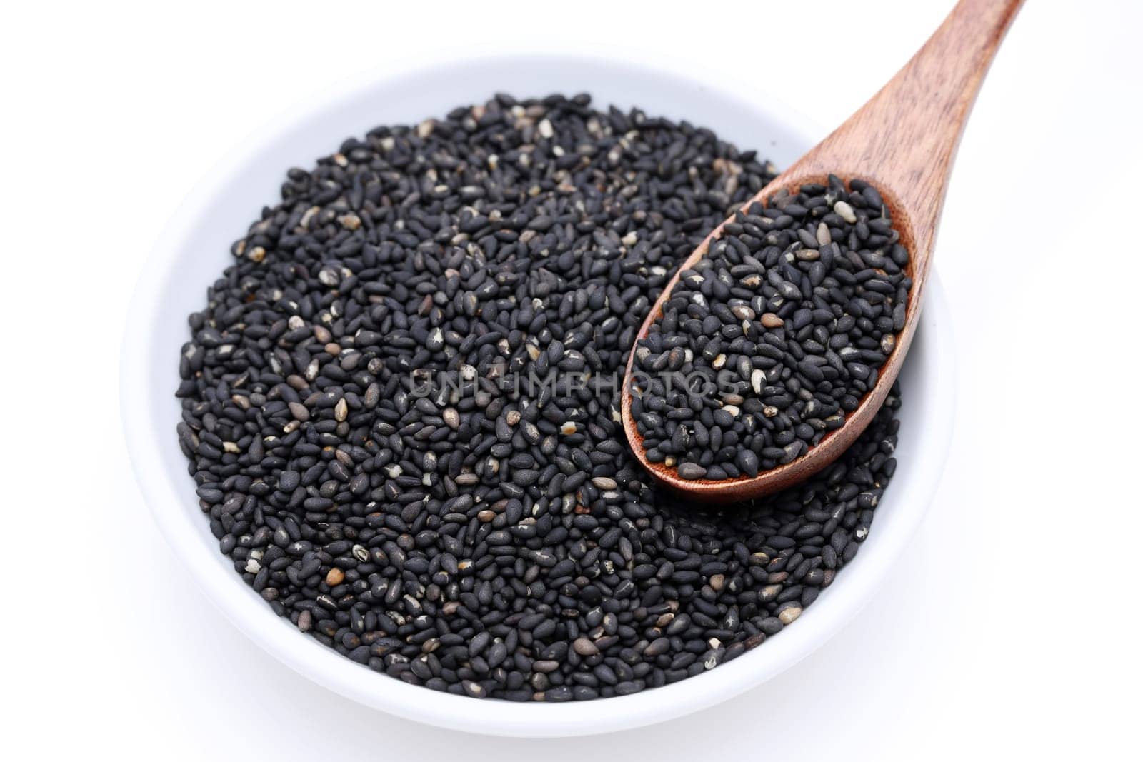 Black sesame seeds with wooden spoon. Sesame seeds in a dish on white background