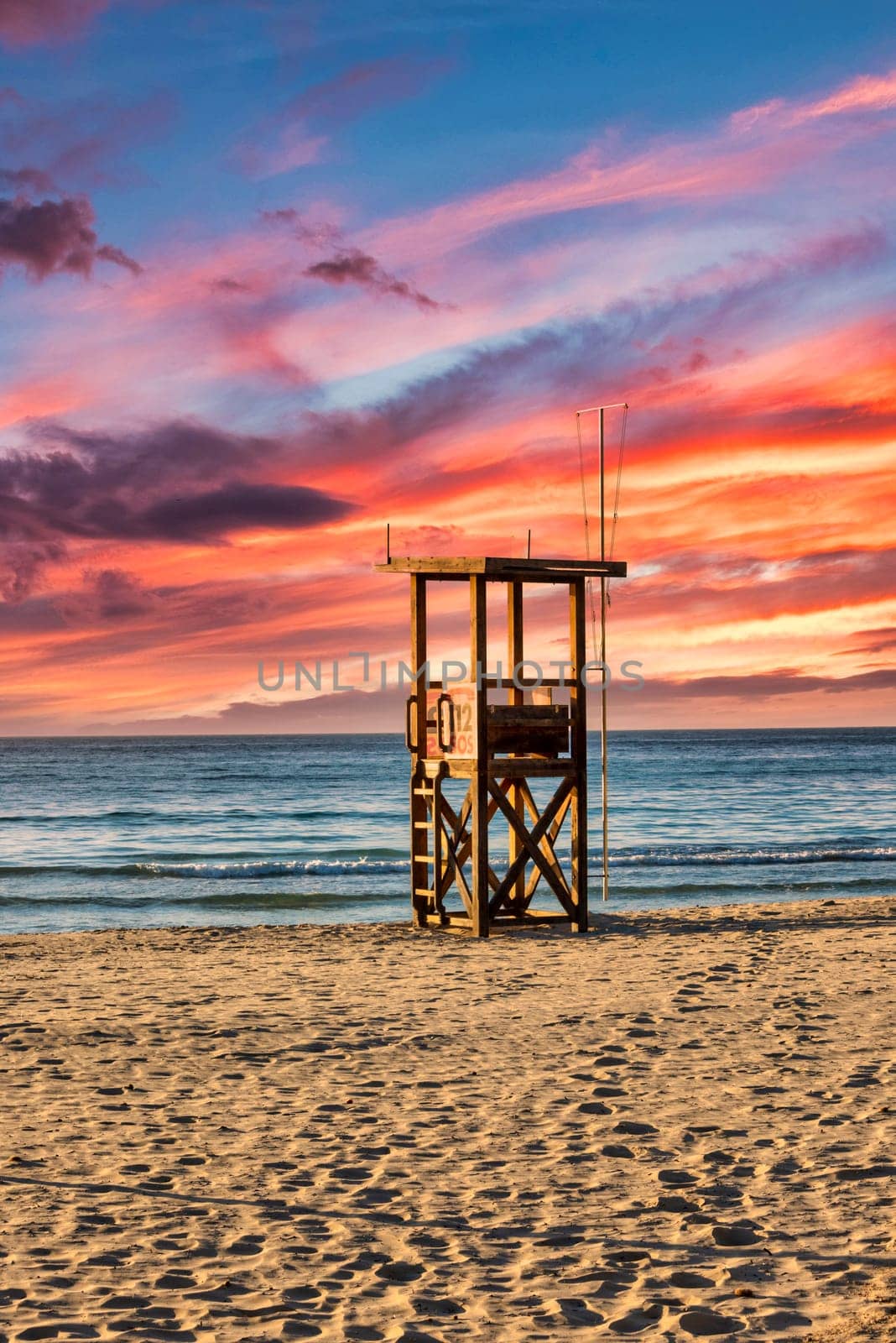 A lifeguard tower stands on the beach on the Mediterranean island of Mallorca with a beautiful colourful sunset