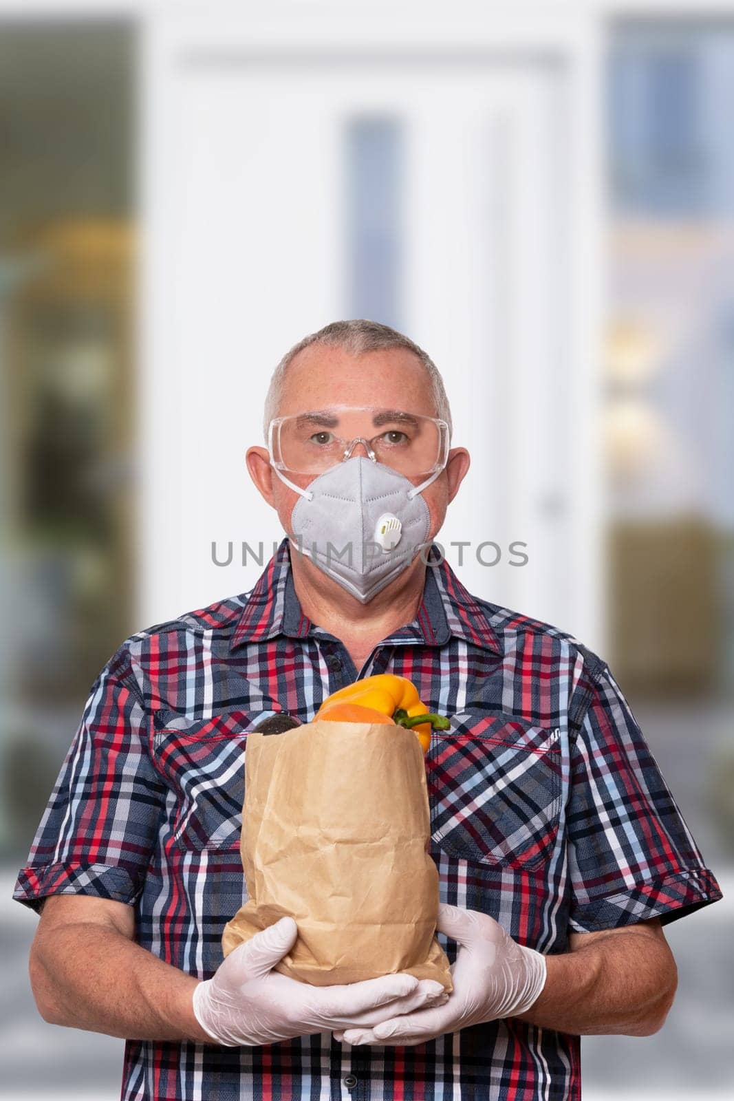Coronavirus protective measures. Man with protective mask, safety goggles and medical gloves comes from a grocery store and carries a bag of fresh vegetables. Avoiding social contact and distance.