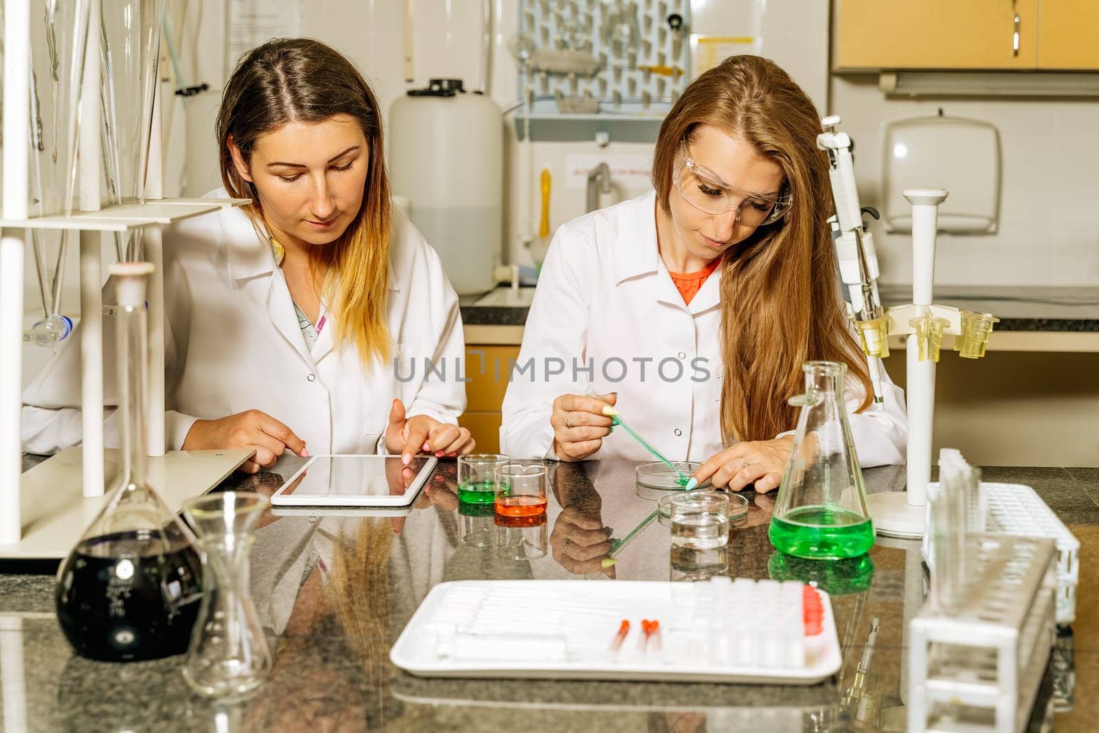 Two female laboratory technicians researching medical samples and reagents for coronavirus or covid 19 vaccination and uploading data through tablet