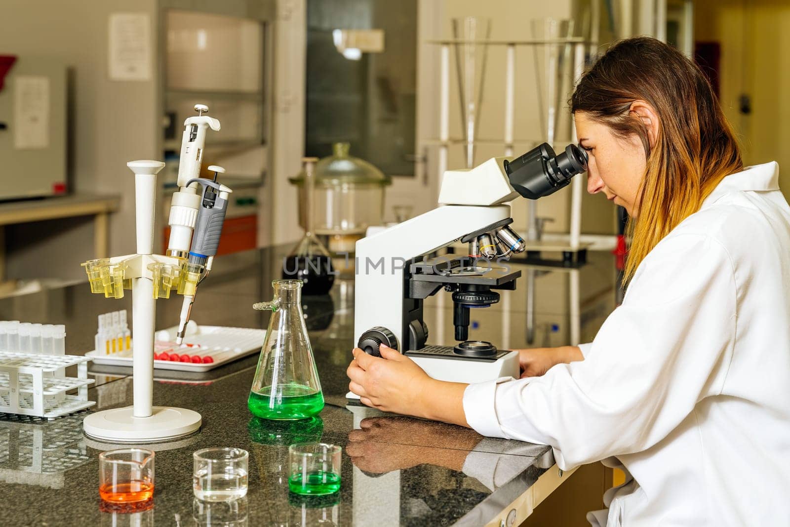 Female doctor or lab technician checking or researching covid 19 virus samples under microscope to help with discovery of coronavirus vaccination