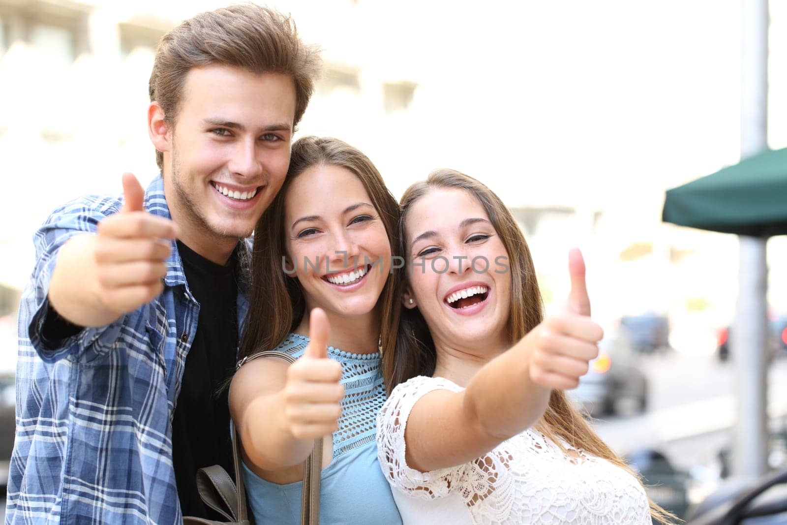 Happy group of three friends with thumbs up and perfect smiles looking camera in the street