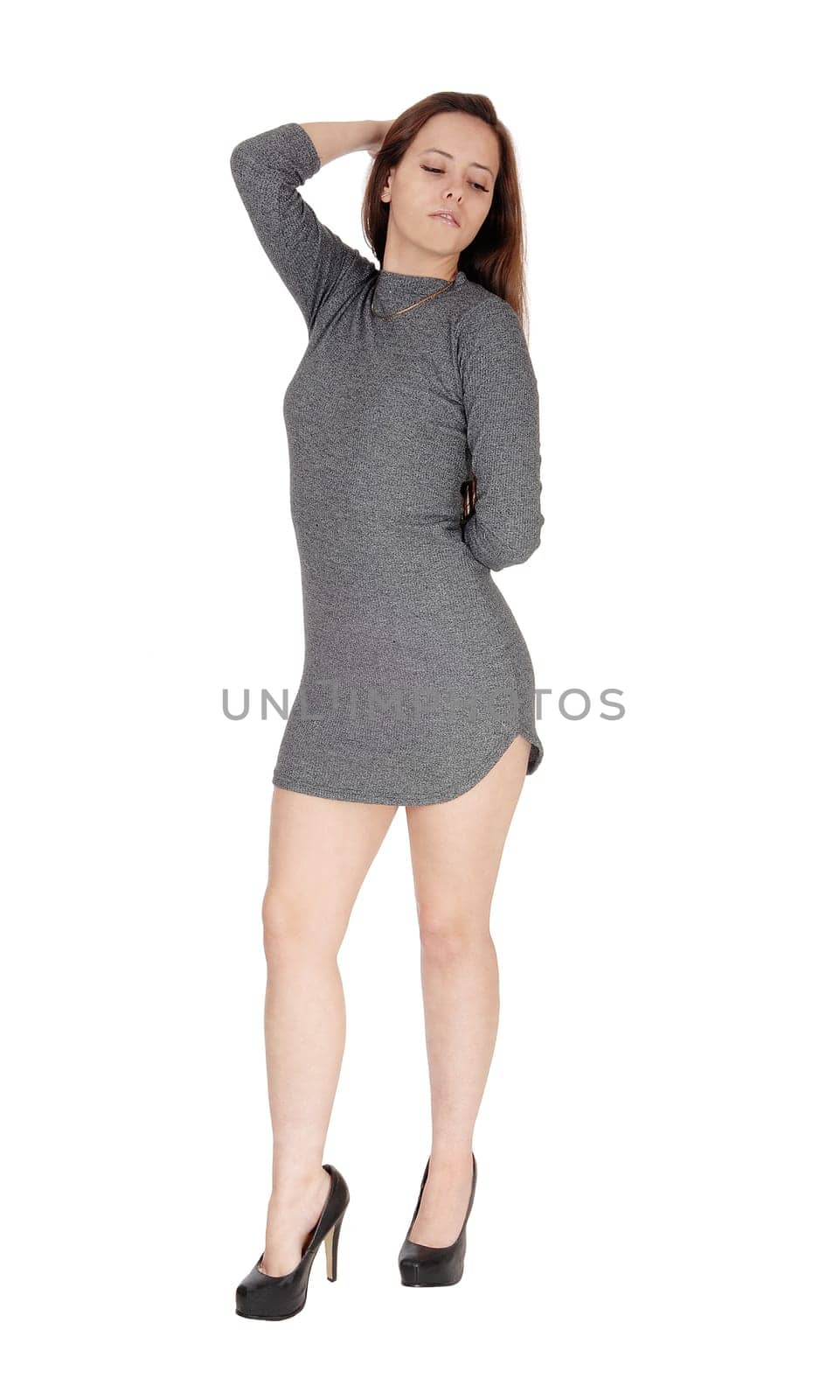A lovely young woman in a gray dress standing with one hand on her.head looking down, isolated for white background.