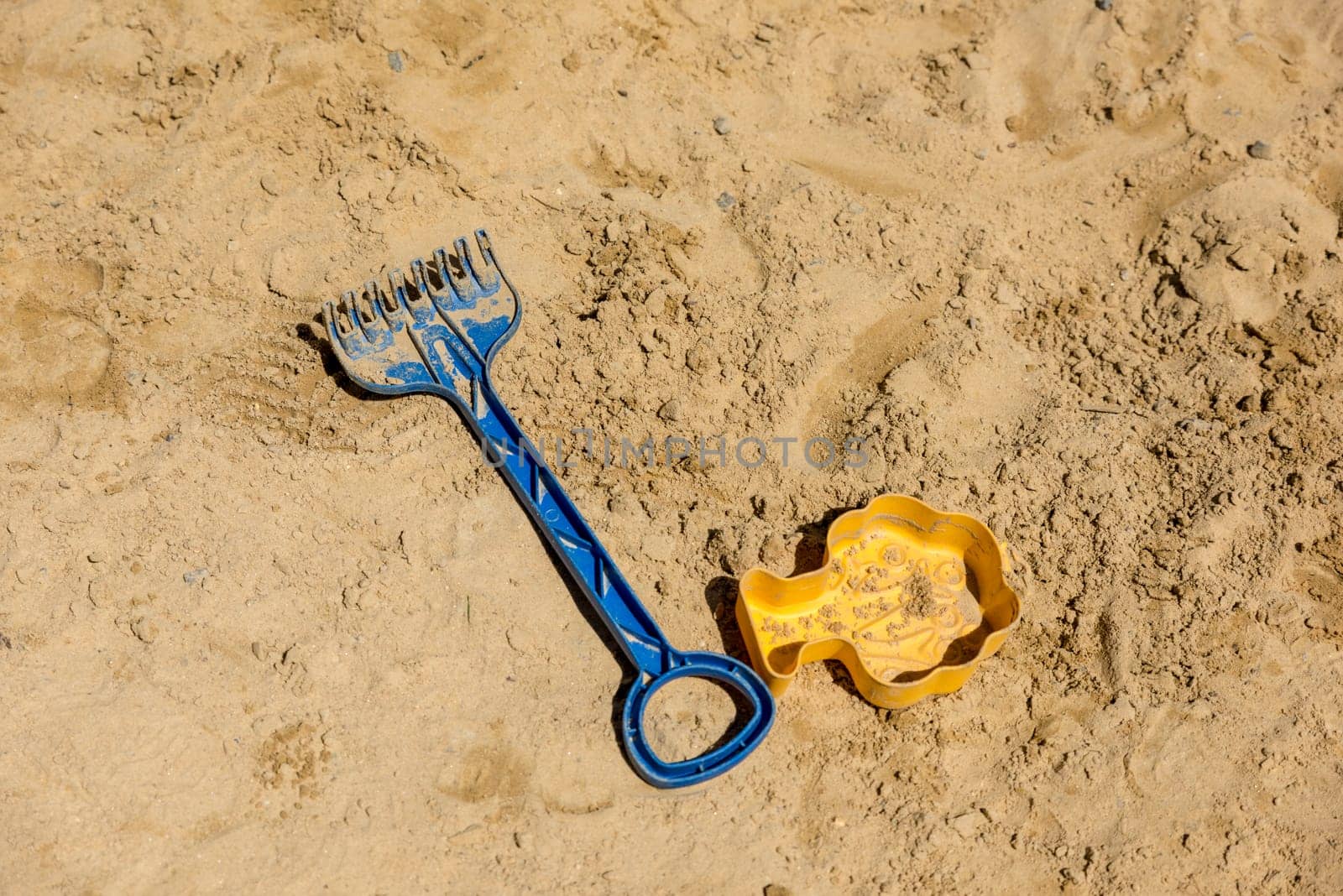Children's toys, shovel and sand mold lie on light sand