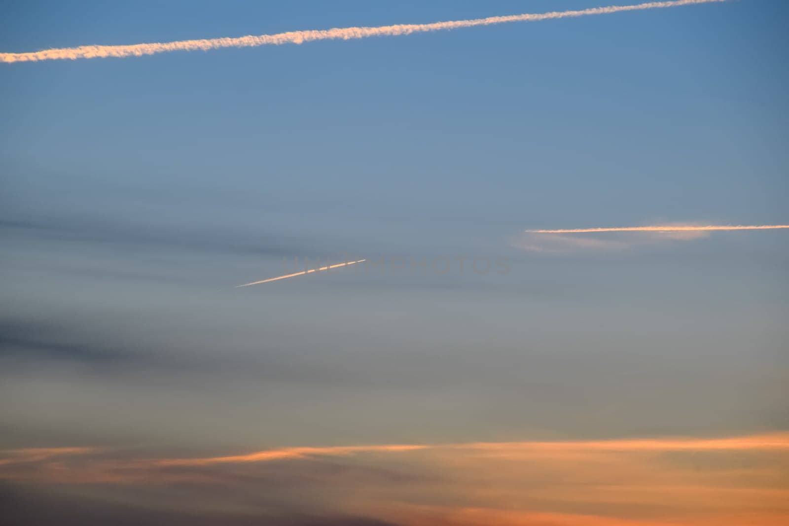 Contrail from an airplane on a blue sky against a sunset.