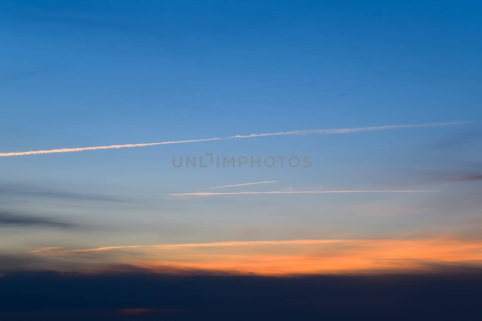 Contrail from an airplane on a blue sky against a sunset.