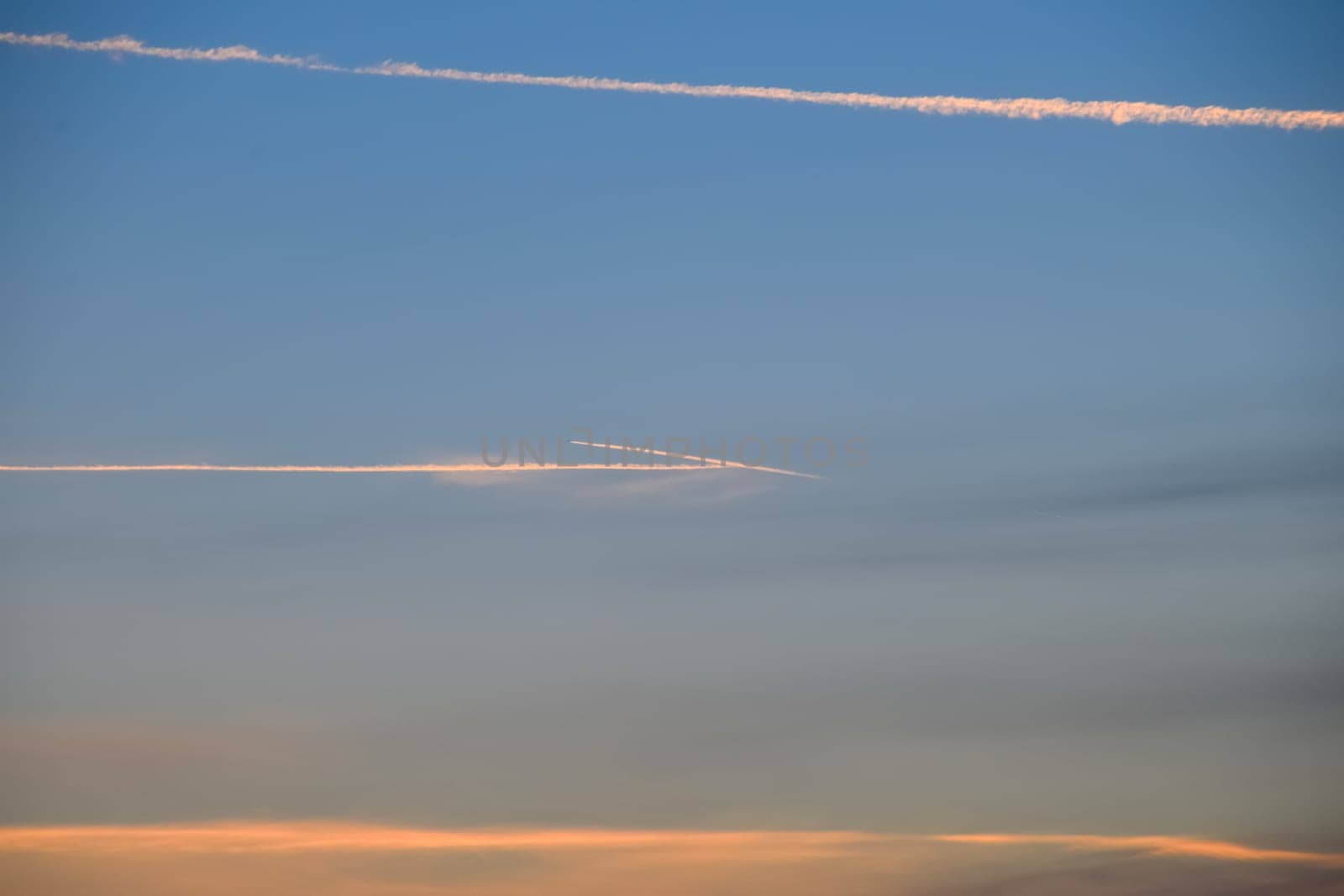 Contrail from an airplane on a blue sky against a sunset.