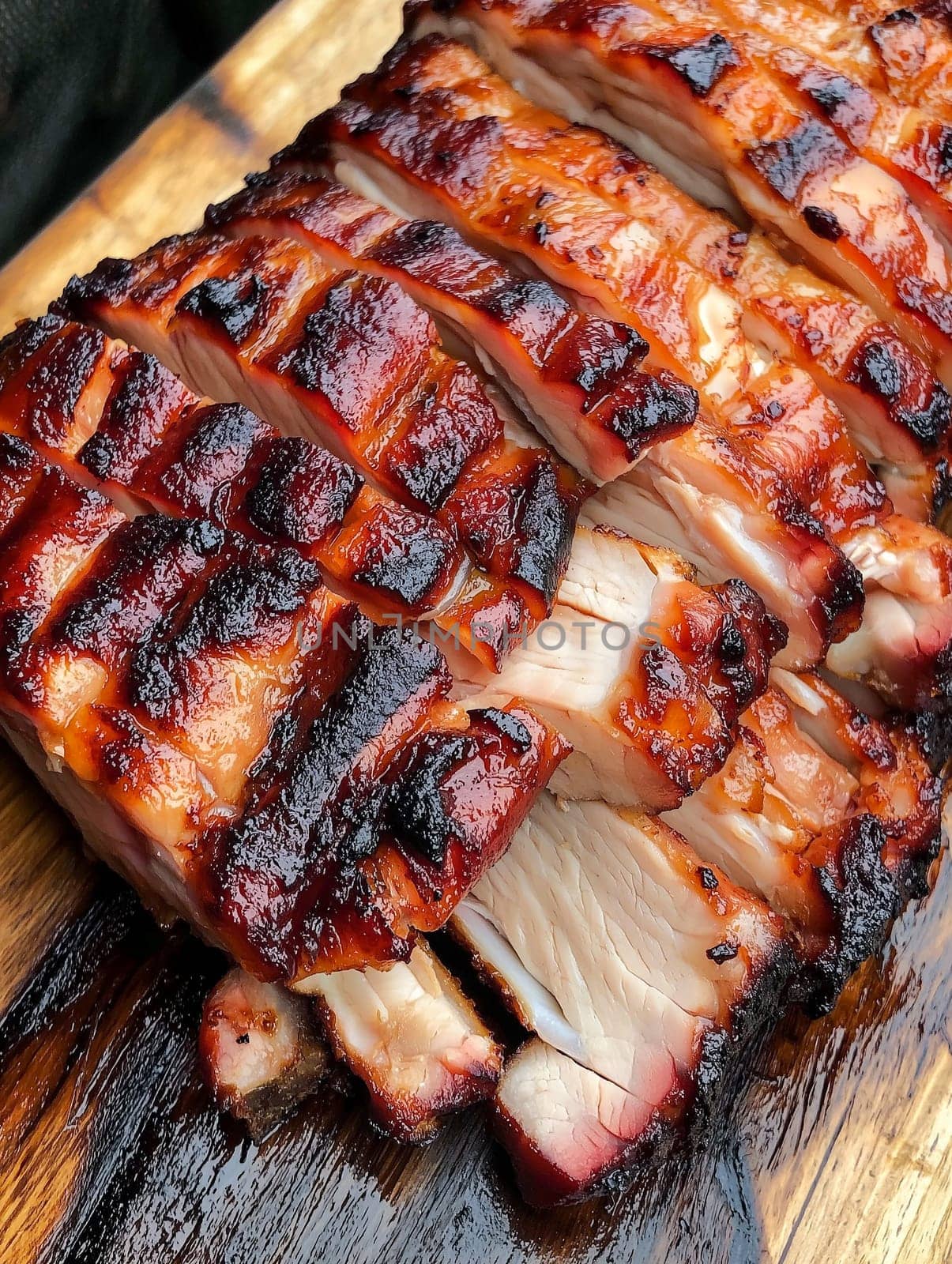 Sliced, glazed pork, likely BBQ'd, sits on a wooden board. The rich color and texture suggest a delicious meal.