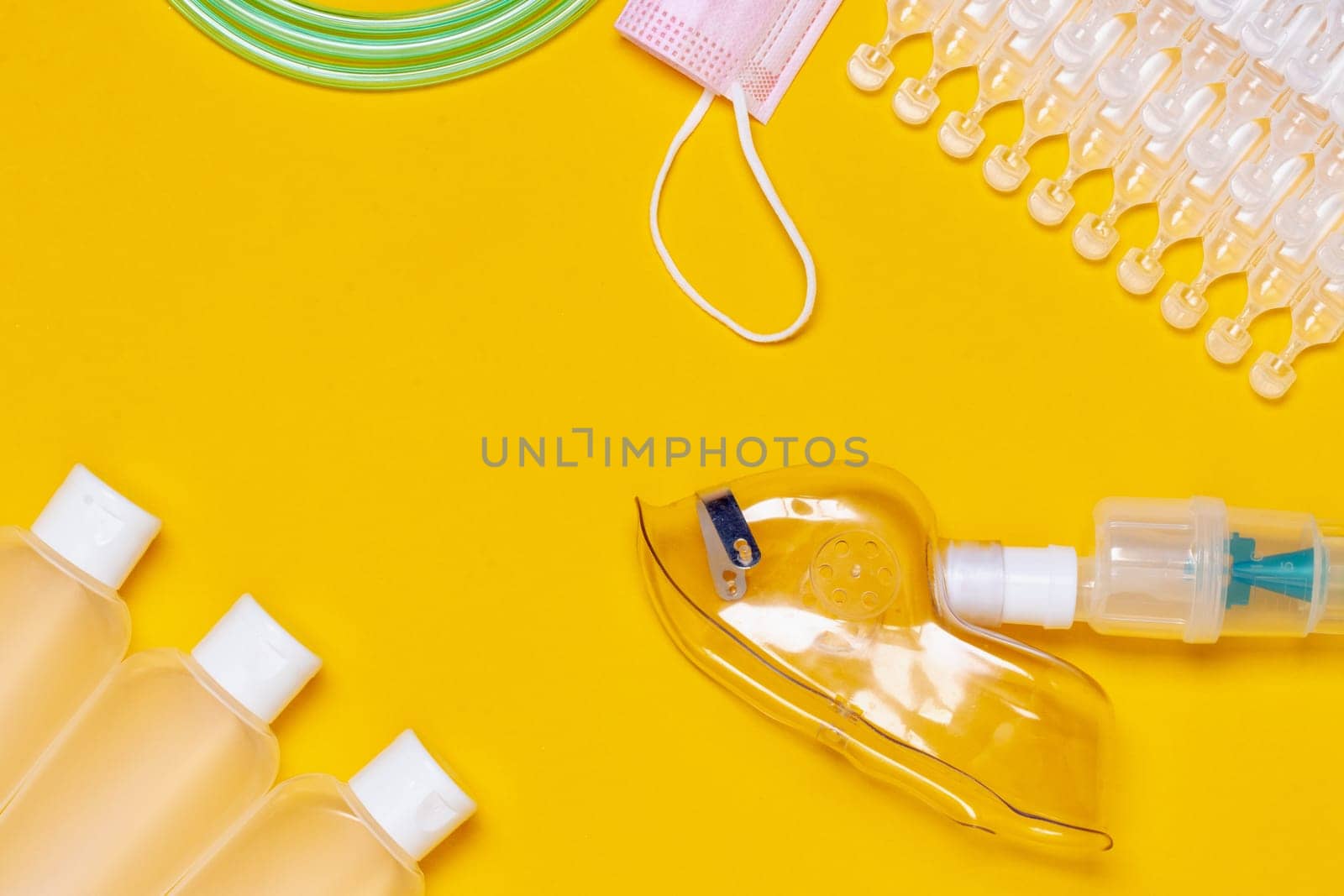 Coronavirus protective measures. Close-up of amedical face mask for treatment of the respiratory tract, ampoules, three bottles of disinfectan and a surgical mask flat layed on a yellow background. Personal protective equipment. Copy space.
