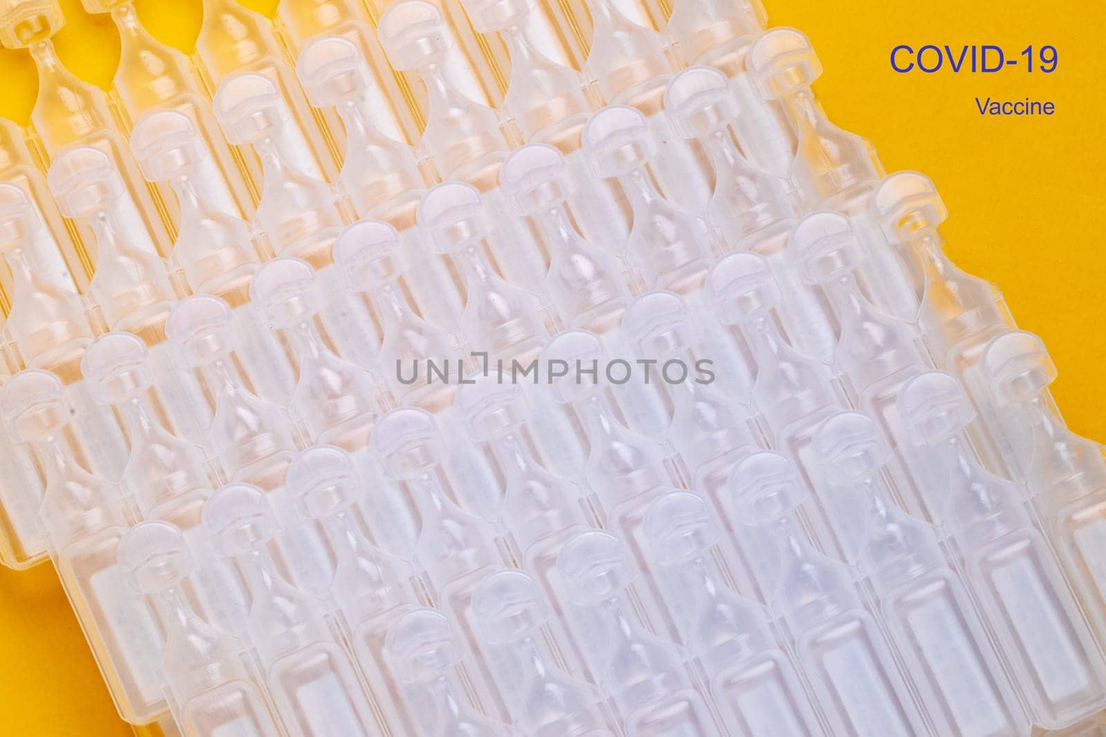 Coronavirus treatment concept. Close-up of a stack several tens packs of ampoules with vaccine COVID-19 flat layed on a yellow background. Global pandemic outbreak and healing the deadly coronavirus.