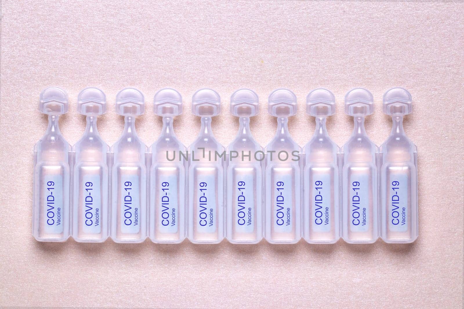 Coronavirus treatment concept. Close-up of ten ampoules with vaccine COVID-19 flat layed on a sparkling light pink paper background. Global pandemic outbreak and healing the deadly coronavirus. Macro photograph.