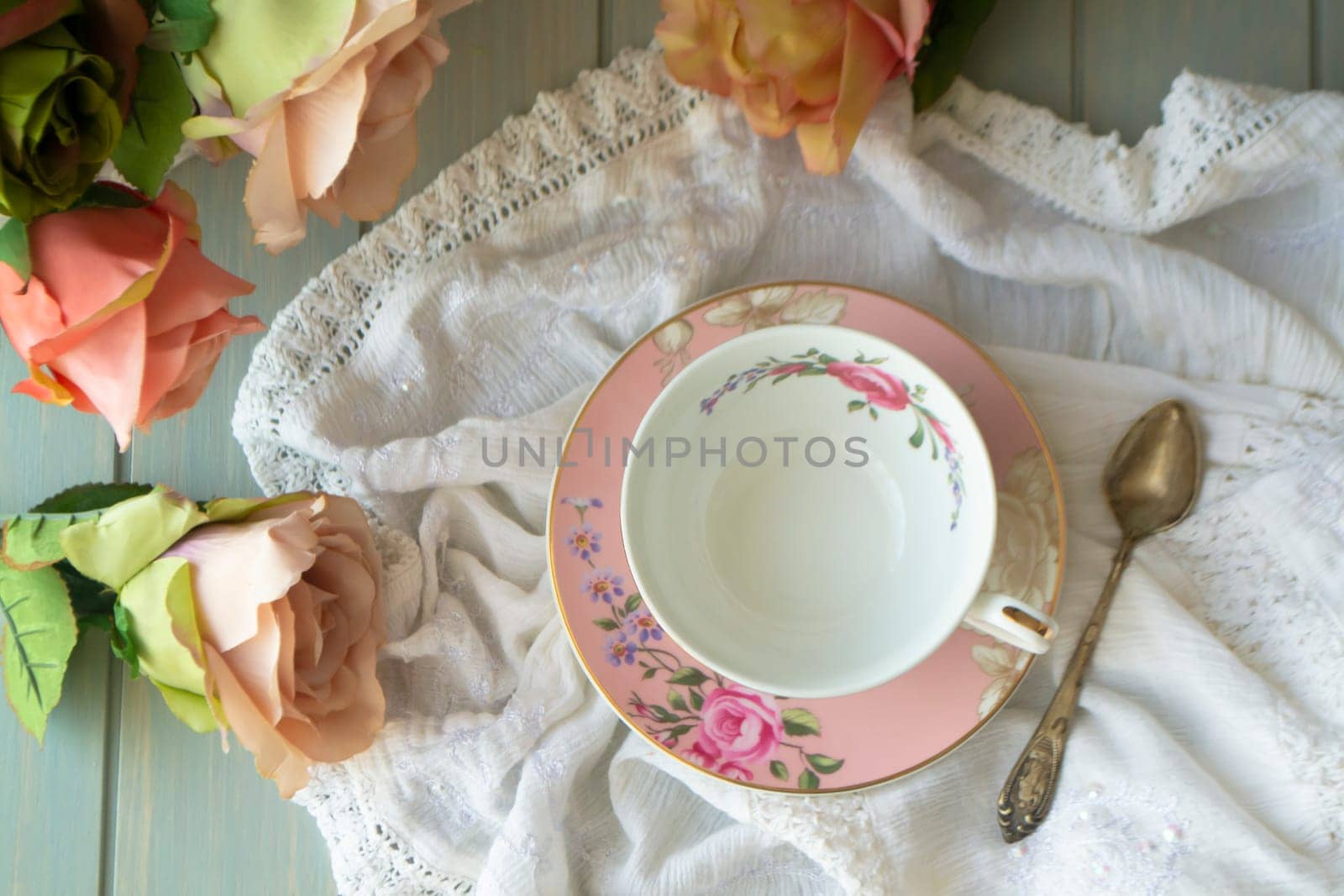 Vintage tea cup with gold rim. White linen tablecloth. Pastel roses, flat lay