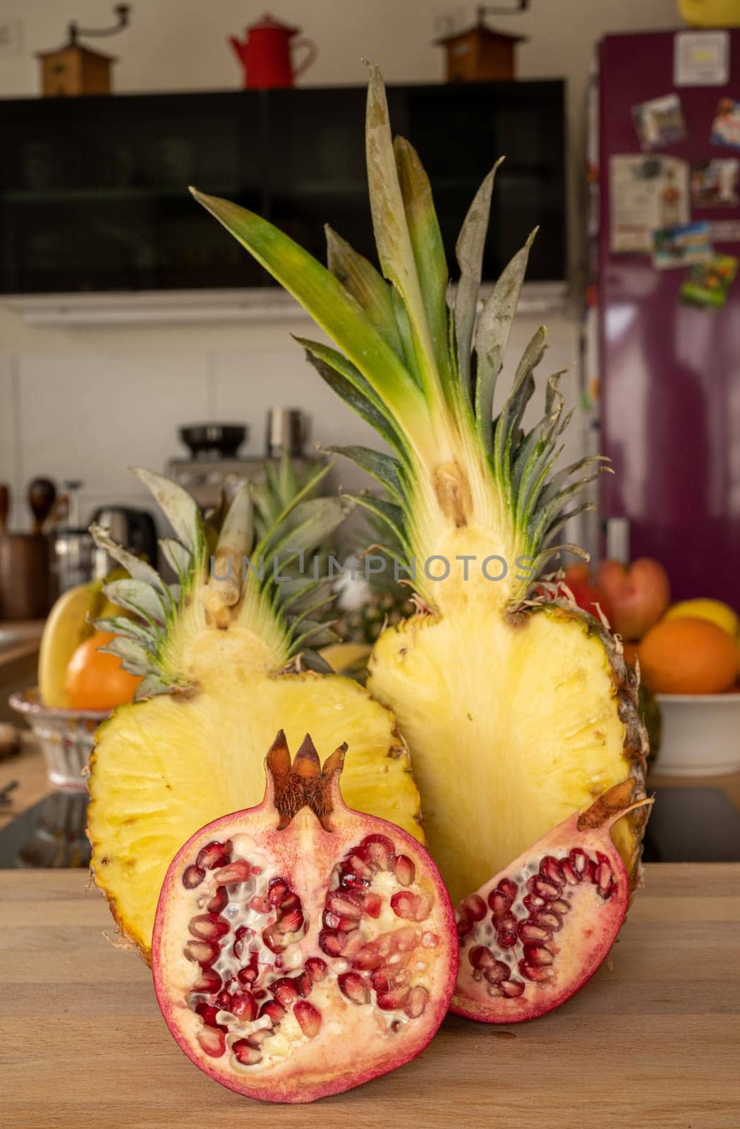 Close-up view of two halve pineapple fruit and a halve Pomegranate fruit on a cutting board in a domestic kitchen with other varieties of fruit in the background