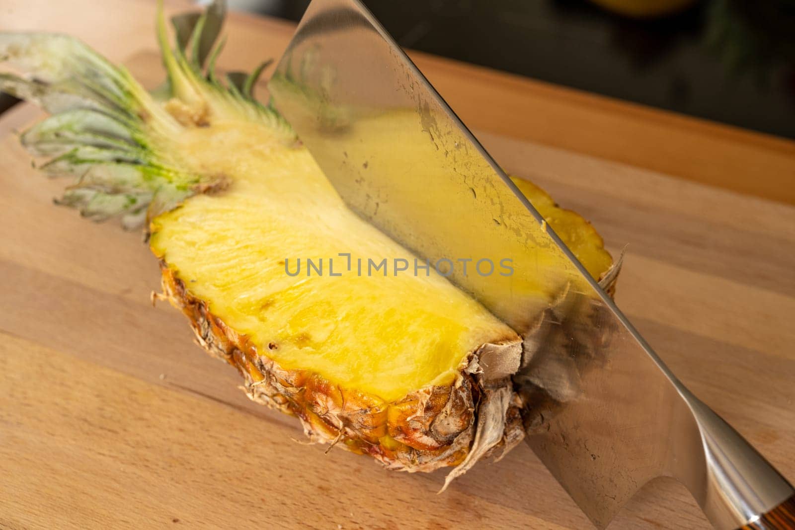Close-up view of a cleaver in half a pineapple fruit on a cutting board in a domestic kitchen
